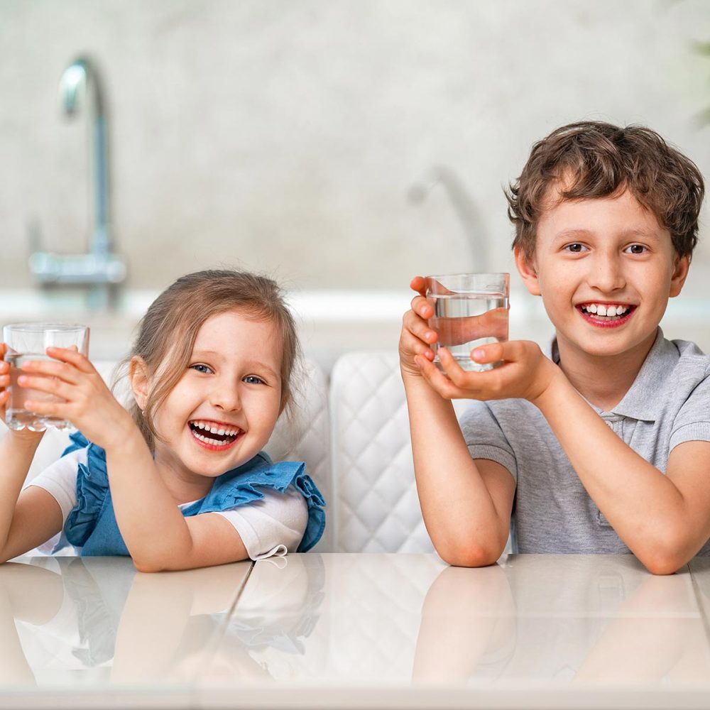 Funny little children drink water in the kitchen at home.